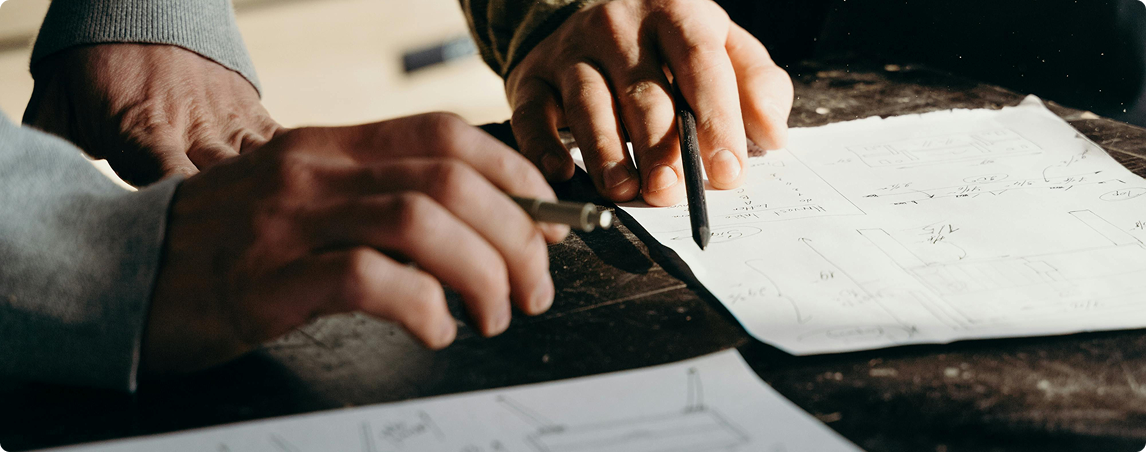 Two hands reviewing sketched design plans and writing with pencils.